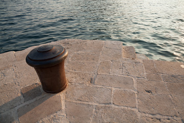 Naklejka premium Old rusted metal bollard stand on stone pier in Montenegro