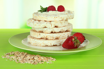 Tasty crispbread with berries on plate, on green table