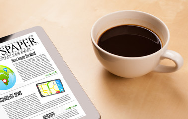 Obraz na płótnie Canvas Tablet pc shows news on screen with a cup of coffee on a desk