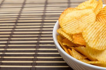 Potato chips in white bowl on bamboo mat