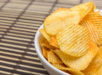 Potato chips in white bowl on bamboo mat