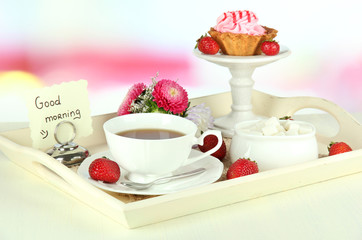 Cup of tea with cakes on wooden tray on table in room