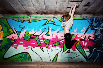 Stylish girl in a dance pose against graffiti wall