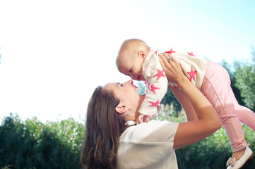 Obraz premium Portrait of a happy young mother lifting cute baby outdoors