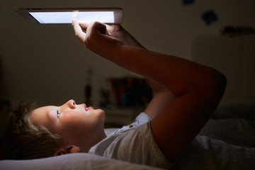 Obraz na płótnie Canvas Boy Looking At Digital Tablet In Bed At Night