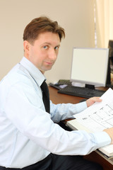 Man wearing white shirt sit at table with drawings of apartment