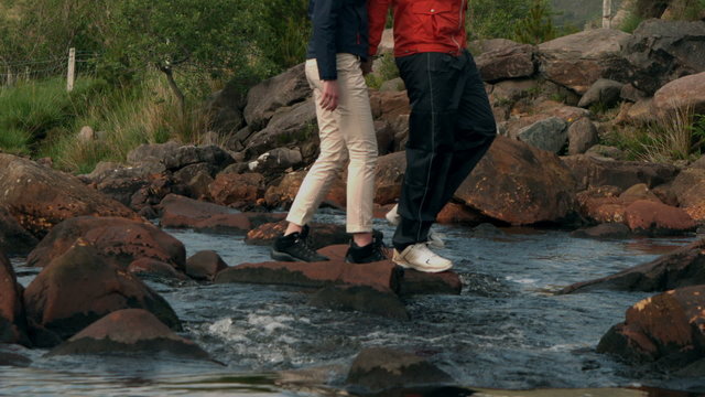 Couple crossing a stream together in the countryside