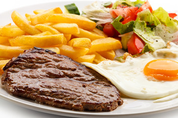 Grilled steaks, French fries, fried egg and vegetables