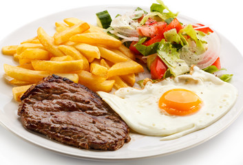 Grilled steaks, French fries, fried egg and vegetables