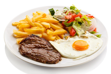 Grilled steaks, French fries, fried egg and vegetables