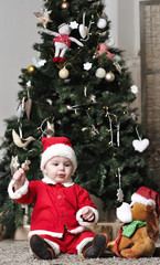 Baby in Santa costume sit near Christmas tree with toy