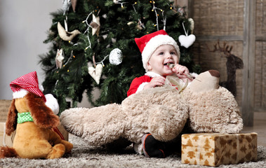 Baby in Santa costume sit near Christmas tree with toys