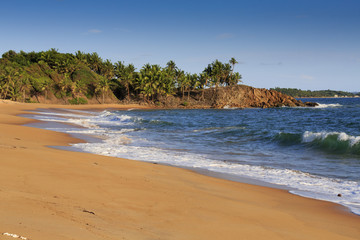Deserted African beach with sand and rocky coastline at sunset