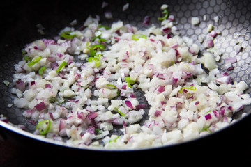 Sliced red and white onion passer in frying pan with green chill