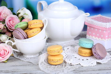 Macaroons in bowl on wooden table on room background