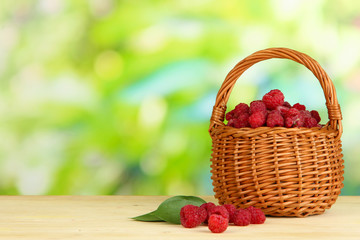 Ripe raspberries in basket on wooden table on natural