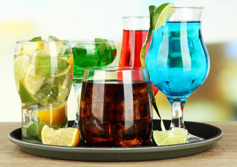Many glasses of cocktails on tray on table, on bright