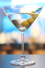 Martini with green olives on table in bar