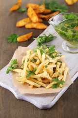 French fries on tracing paper on board on wooden table