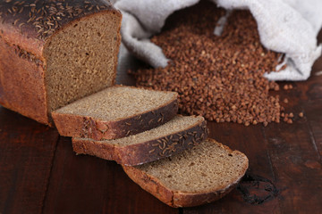 Cloth bag with buckwheat and bread on wooden background