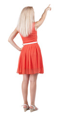 Back view of young blonde woman pointing at wall.