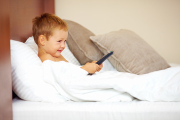 happy kid watching tv cartoons in bed