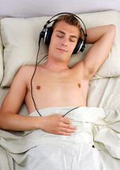 Hombre joven escuchando música en la cama.