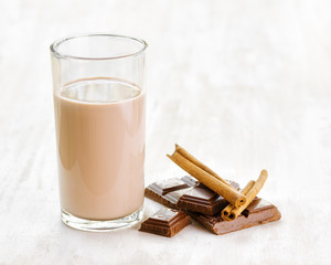 Chocolate milk with chocolate and cinnamon on white wooden table