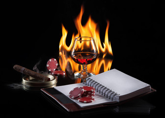 glass of cognac with poker markers, notebook and cigar in fire f