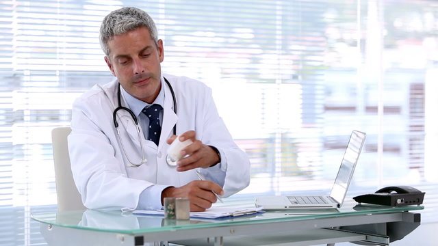 Doctor looking at pills while writing a prescription