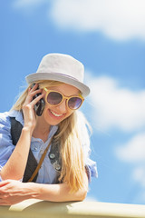 Smiling hipster girl talking mobile phone against sky