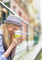 Smiling hipster girl with cup of hot beverage on city street