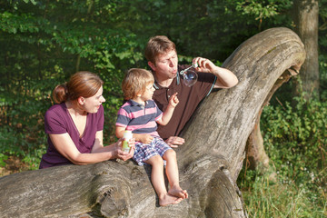 Family of three blowing soap bubbles together in summer forest