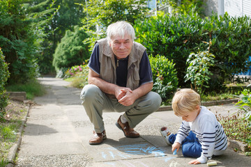 Little blond toddler boy and happy grandfather painting with cha
