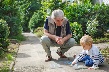 Little blond toddler boy and happy grandfather painting with cha