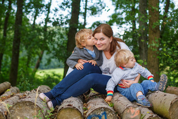 Naklejka na ściany i meble Young mother and two little boys having fun in summer forest.