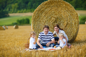 Naklejka na ściany i meble happy family of four picnicking on yellow hay field in summer.