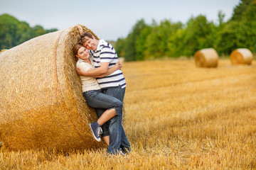 Young couple in love on yellow hay field on summer evening.