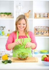 Obraz na płótnie Canvas Happy smiling woman in kitchen preparing vegetable salad