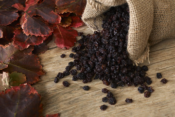 Black raisins in burlap bag over wooden table