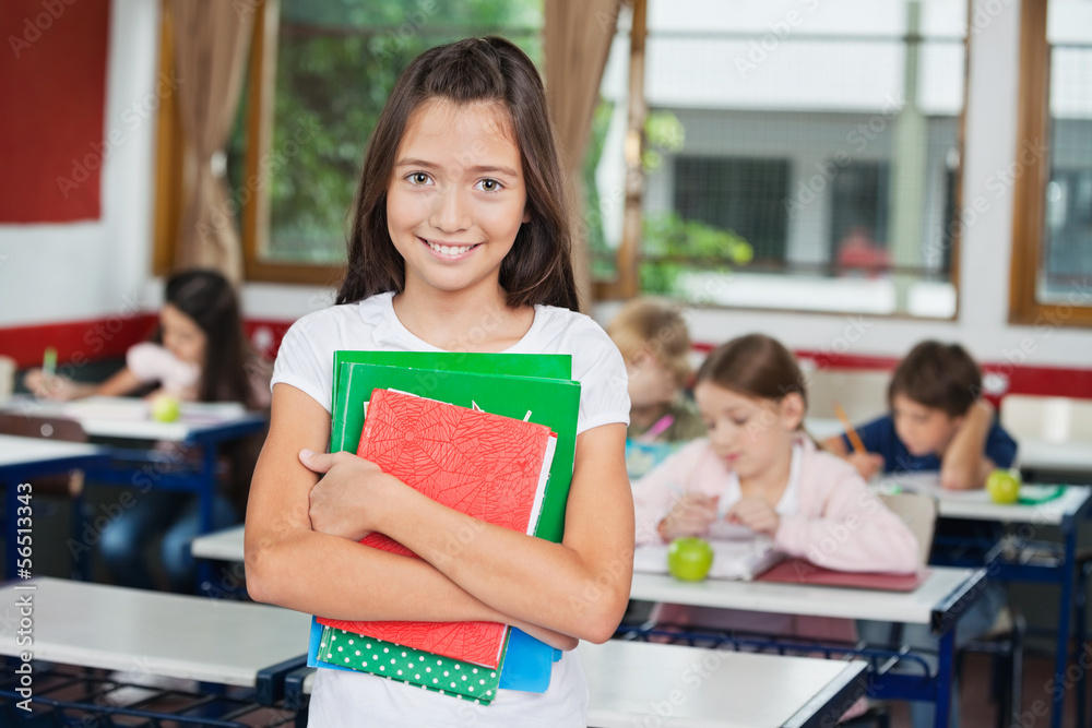 Wall mural schoolgirl holding books while standing at desk