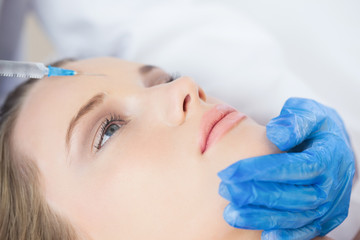 Obraz na płótnie Canvas Surgeon making injection on forehead on calm woman lying