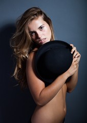 Naked woman in lingerie covering breast with hat