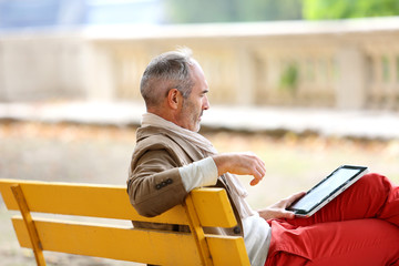 Trendy senior man relaxing on bench with tablet