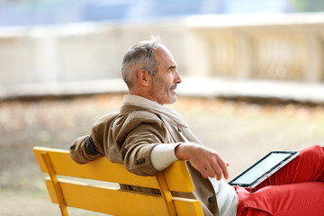 Trendy senior man relaxing on bench with tablet