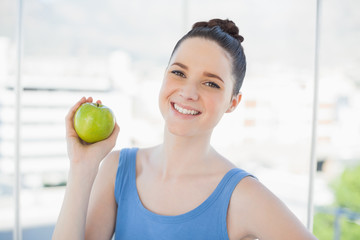 Cheerful slender woman in sportswear holding green apple