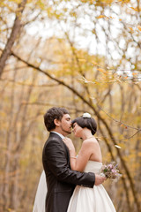 Kissing bride and groom in their wedding day near autumn tree 