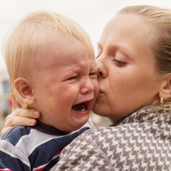 Portrait of a crying little boy who is being held by her mother