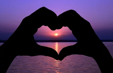 Papier Peint photo Mer / coucher de soleil Woman's hand united forming a heart shape symbol at sunset