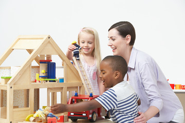 Pre-School Teacher And Pupils Playing With Wooden House